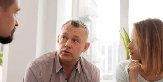 Group of three people sat close together having a conversation in front of a window