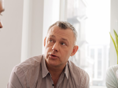 Group of three people sat close together having a conversation in front of a window