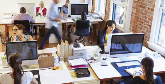 Office workers using display screen equipment at adjustable desks in an open-plan office
