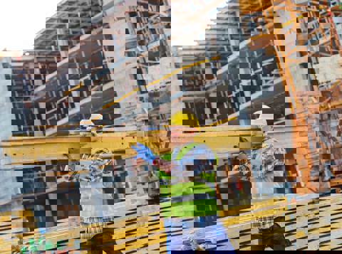 Man on construction site wearing high vis and other PPE carrying steel beam