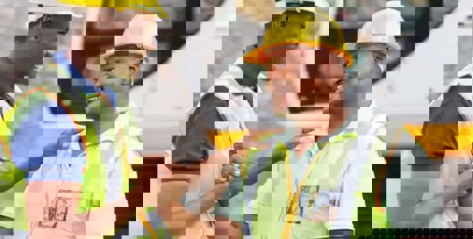 Two men in hard hats and high vis greeting each other with a smile and a handshake