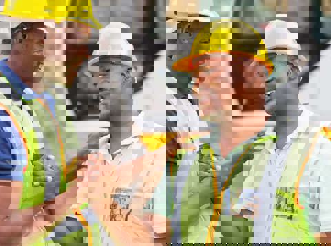 Two men in hard hats and high vis greeting each other with a smile and a handshake
