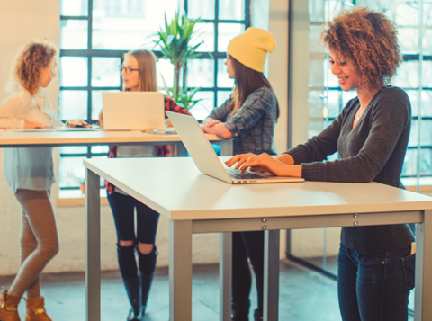 Four women working at standing desks in a modern office