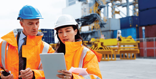 British Safety Council Consultancy Services - Man and woman on work site in hard hats and high visibility jackets looking at an i-pad
