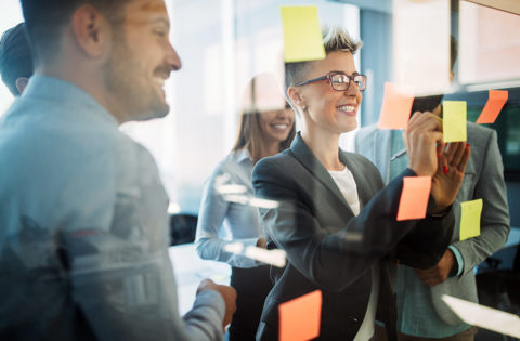 Colleagues smiling and adding sticky notes to a glass wall during a planning session