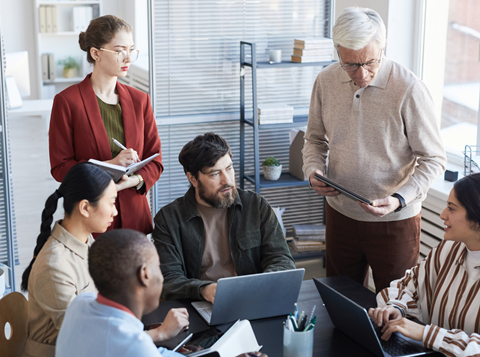 A diverse group of people working together in an office room around a table.