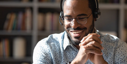 Man wearing headset smiling into distance with hands interlocked