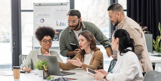 Five people sat around a laptop working together in a modern office