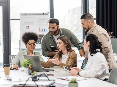 Five people sat around a laptop working together in a modern office