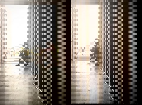 Construction worker sat alone in a shipping container with his head in his hands looking sad