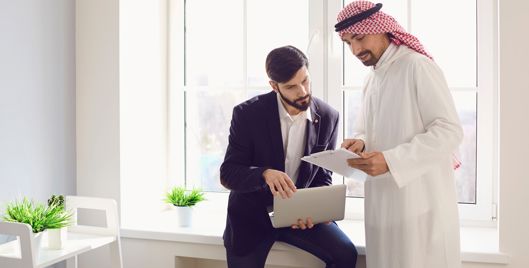 Two men in an office discussing documents on a laptop