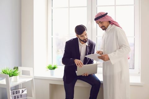 Two men in an office discussing documents on a laptop