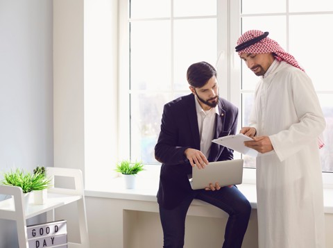 Two men in an office discussing documents on a laptop