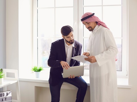 Two men in an office discussing documents on a laptop