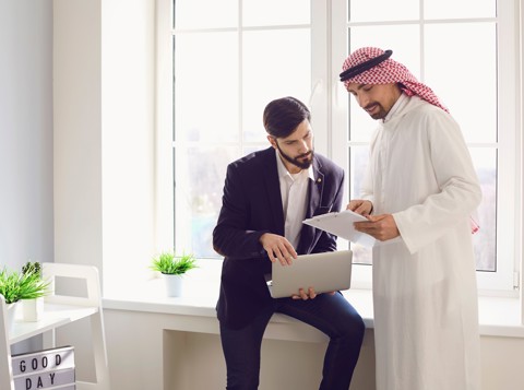 Two men in an office discussing documents on a laptop