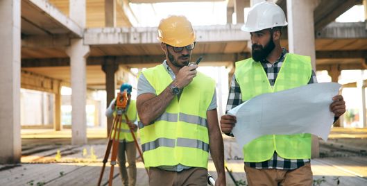 Two construction workers wearing PPE looking at plans on a construction site