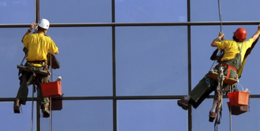 Two people wearing PPE and using safety equipment cleaning windows