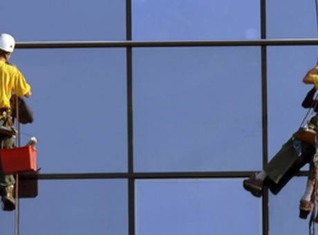 Two people wearing PPE and using safety equipment cleaning windows