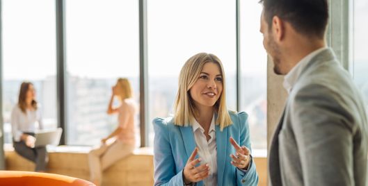 Man and woman having a discussion in front of a large, bright office window