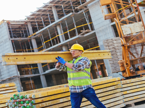 Man on construction site wearing high vis and other PPE carrying steel beam