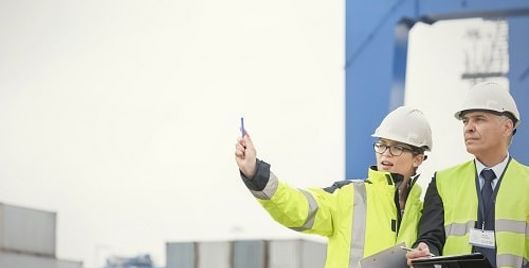 Two people wearing high vis and hard hats holding a clipboard at a site