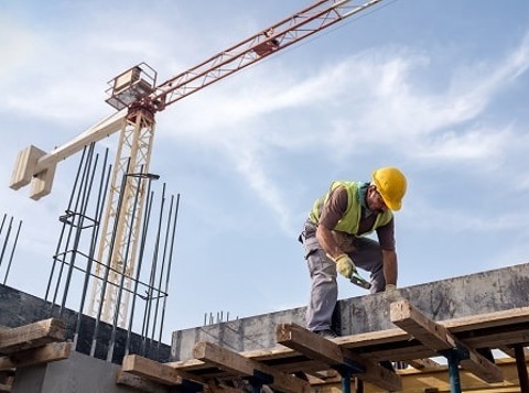 Man wearing PPE working on construction site with a crane in the background