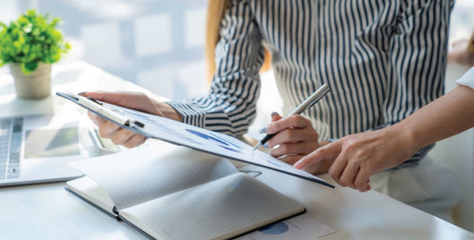 Woman working at desk and looking at a clipboard with colleague
