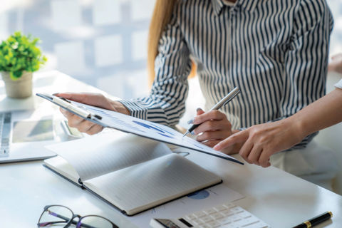 Woman working at desk and looking at a clipboard with colleague