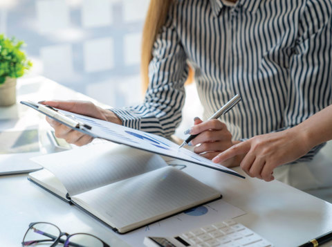 Woman working at desk and looking at a clipboard with colleague