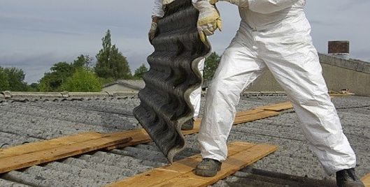 Worker removing asbestos sheets from a roof while wearing PPE