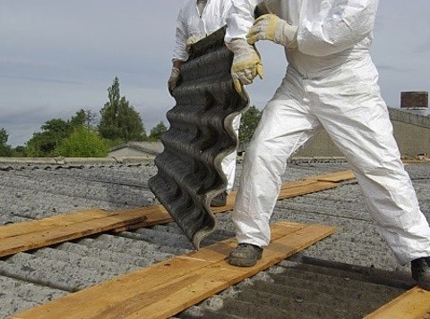 Worker removing asbestos sheets from a roof while wearing PPE