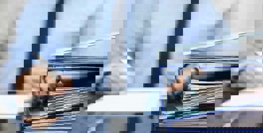 Man in business attire writing notes with a binder on the desk in front of him