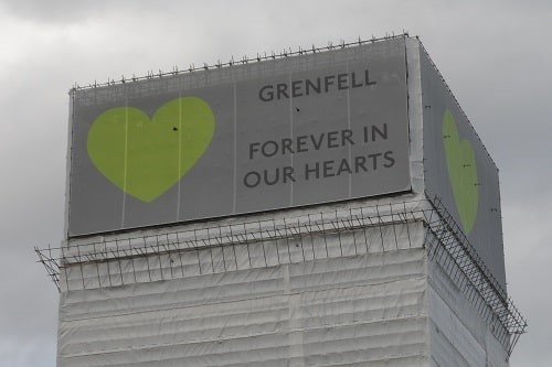Grenfell Tower with banners at the top with heart symbol and the wording "Grenfell Forever In Our Hearts" in June 2018. Photograph: Carcharoth / Wikimedia