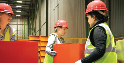 Three people wearing hard hats and hi vis lifting red boxes in a warehouse