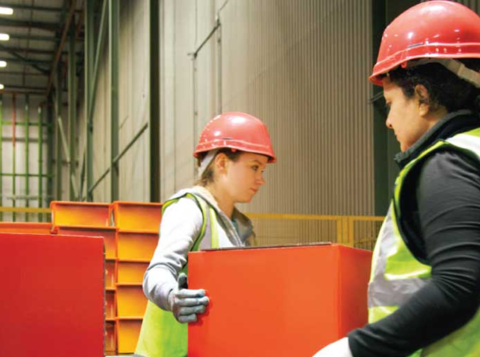 Three people wearing hard hats and hi vis lifting red boxes in a warehouse